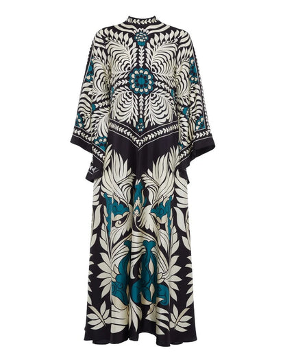 Multi - A woman wearing a high-neck maxi dress with a bold engineered botanical print in black, cream, and teal, featuring wide cape sleeves and a fluid, floor-length drape.