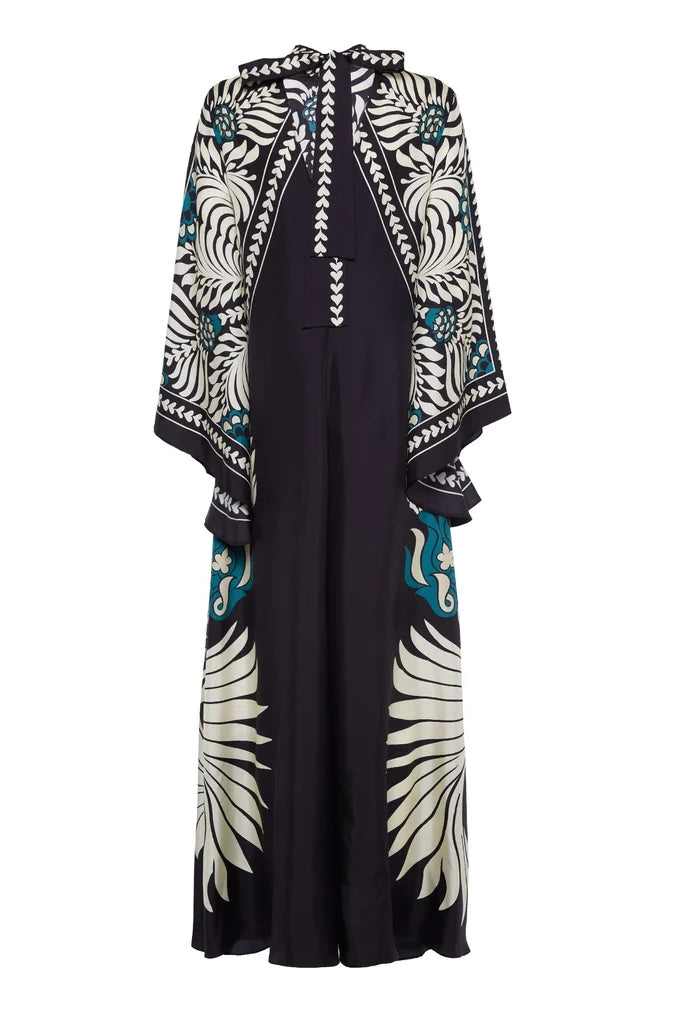 Multi - A woman wearing a high-neck maxi dress with a bold engineered botanical print in black, cream, and teal, featuring wide cape sleeves and a fluid, floor-length drape.