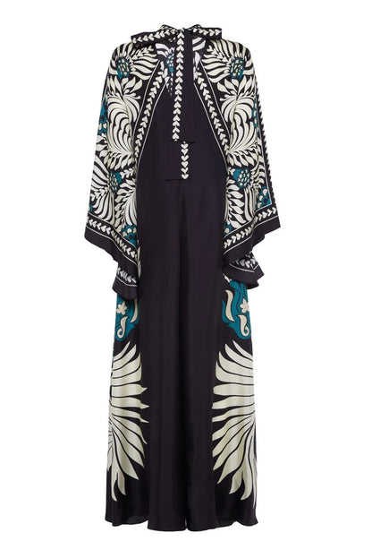Multi - A woman wearing a high-neck maxi dress with a bold engineered botanical print in black, cream, and teal, featuring wide cape sleeves and a fluid, floor-length drape.