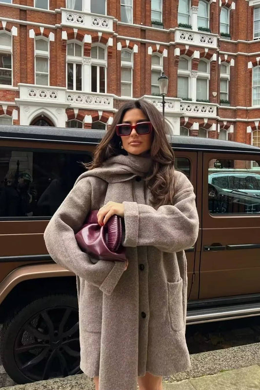 Khaki - A woman wearing a taupe brushed wool mid-length coat with an integrated matching scarf, styled with dark sunglasses and a plum clutch against a classic brick building background.