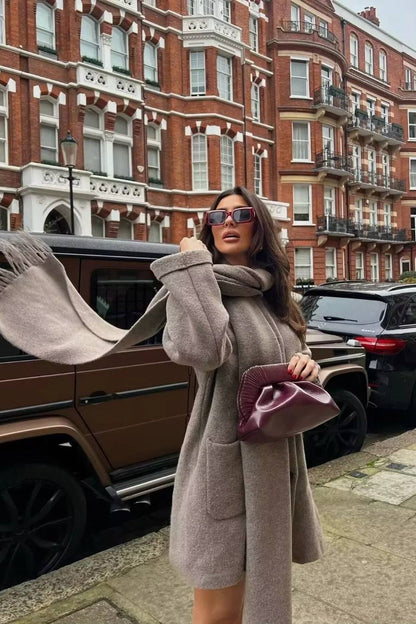 Khaki - A woman wearing a taupe brushed wool mid-length coat with an integrated matching scarf, styled with dark sunglasses and a plum clutch against a classic brick building background.