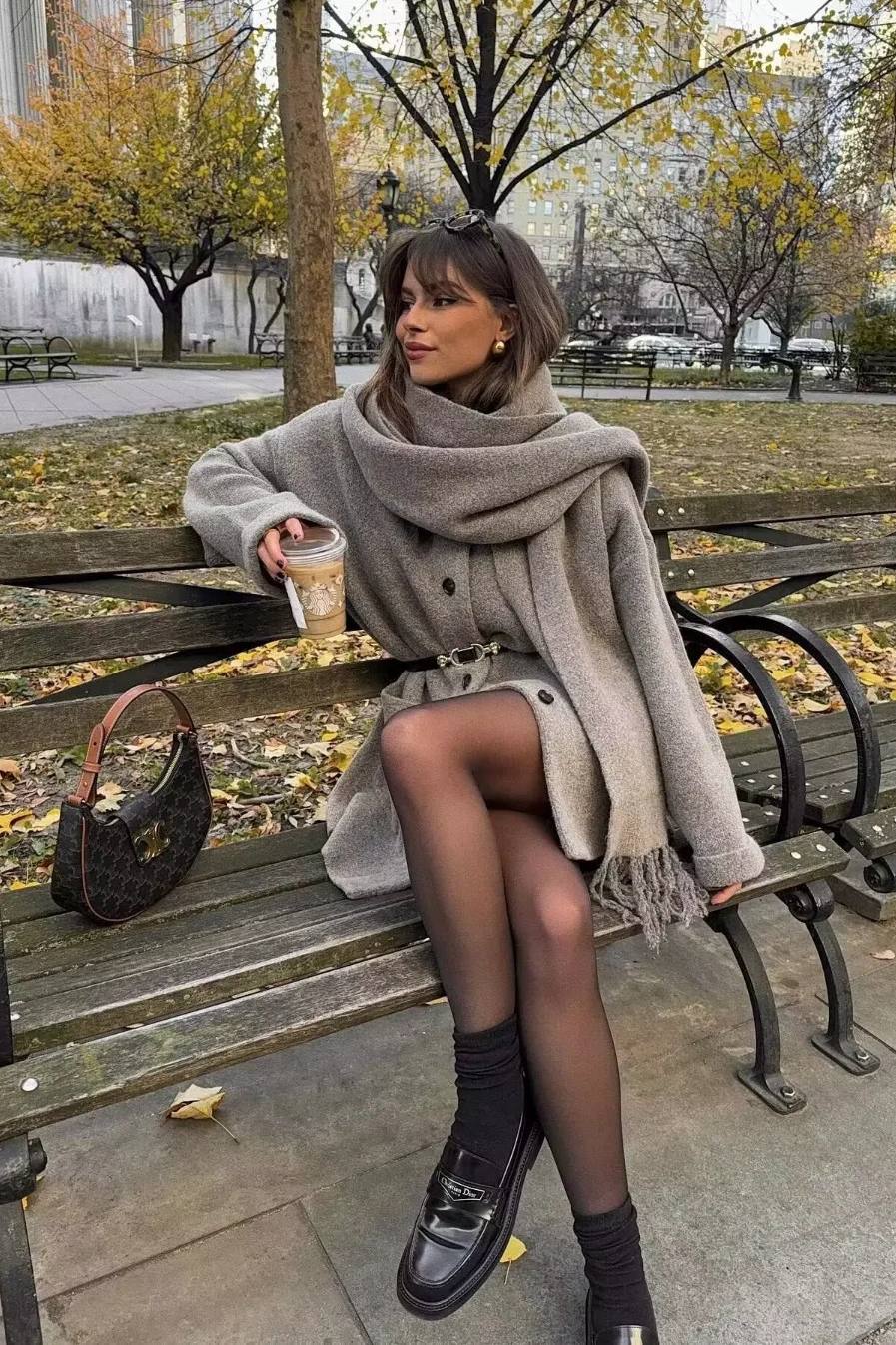 Khaki - A woman wearing a taupe brushed wool mid-length coat with an integrated matching scarf, styled with dark sunglasses and a plum clutch against a classic brick building background.