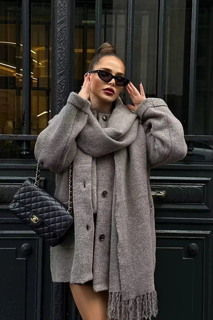 Grey - A woman wearing a taupe brushed wool mid-length coat with an integrated matching scarf, styled with dark sunglasses and a plum clutch against a classic brick building background.