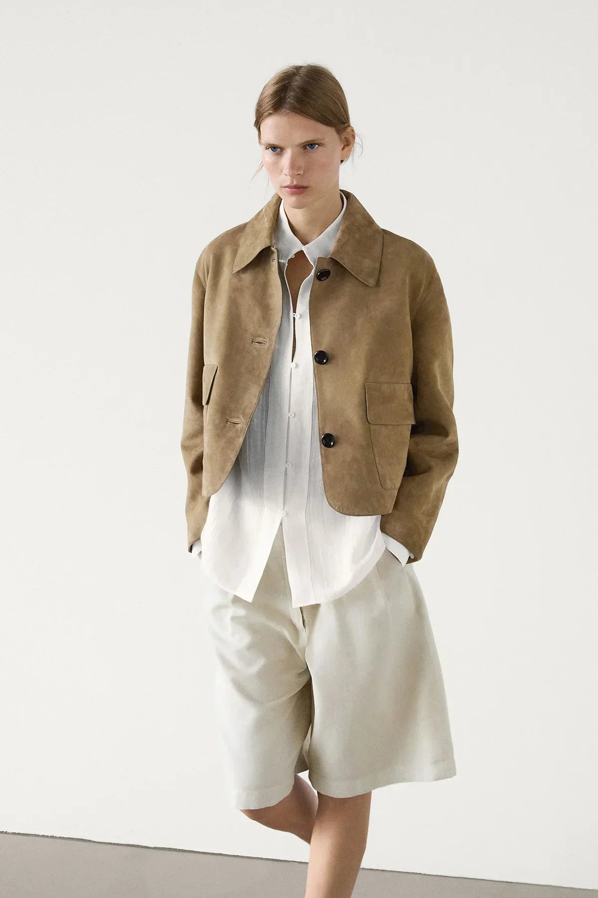 sand - Women's tan suede-look cropped jacket featuring a point collar, large button closures, and two front flap pockets, styled over white tailored shorts.