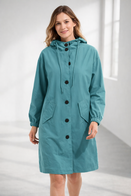 Turquoise - A woman wearing a teal mid-length hooded coat with a contrast black button-down front, angled flap pockets, and elasticated cuffs, set against a bright minimalist interior.