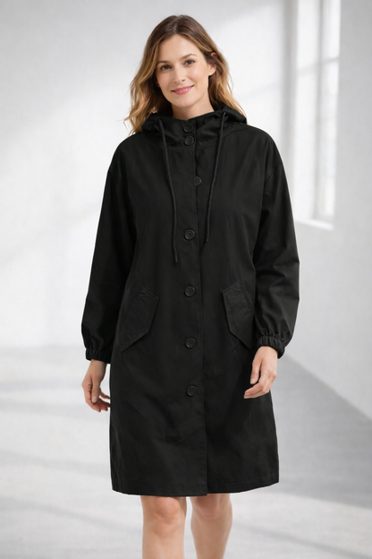 Black - A woman wearing a teal mid-length hooded coat with a contrast black button-down front, angled flap pockets, and elasticated cuffs, set against a bright minimalist interior.