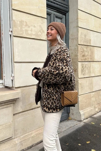A woman wearing a relaxed-fit, fuzzy knit cardigan featuring a bold leopard print and contrasting dark ribbed placket, styled open over a white top and blue jeans.