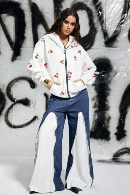 White - A woman wearing a white, oversized zip-up hoodie featuring a scattered red cherry print, paired with unique denim trousers.