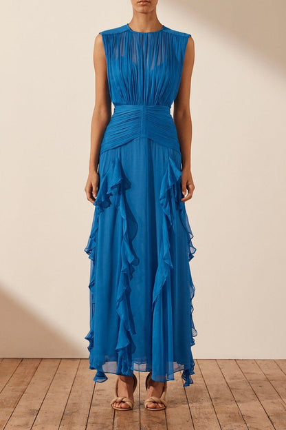 Blue - A woman wearing a vibrant cobalt blue sleeveless chiffon maxi dress featuring a high gathered neckline, a wide ruched waistband, and cascading vertical ruffles along the skirt.