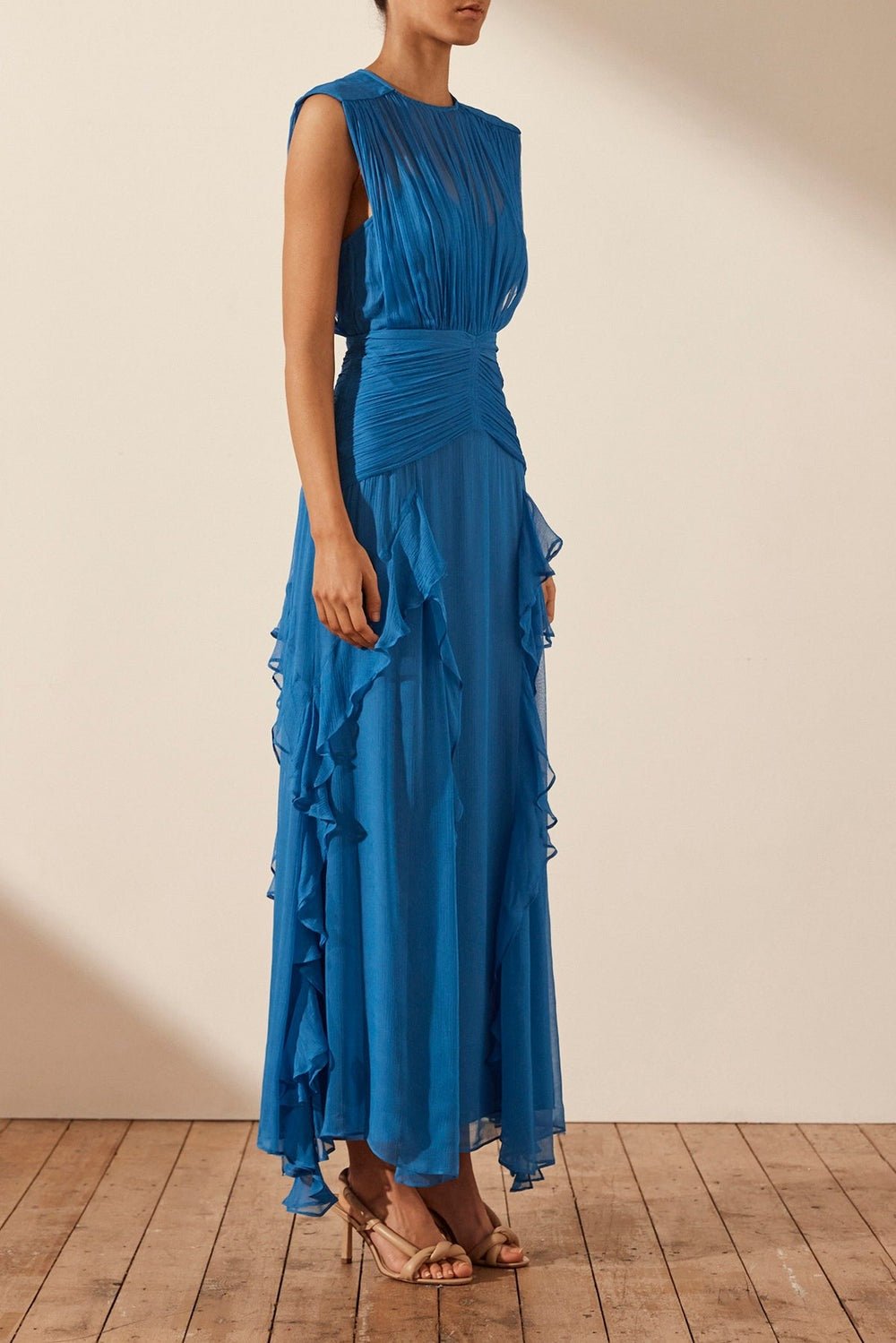 Blue - A woman wearing a vibrant cobalt blue sleeveless chiffon maxi dress featuring a high gathered neckline, a wide ruched waistband, and cascading vertical ruffles along the skirt.