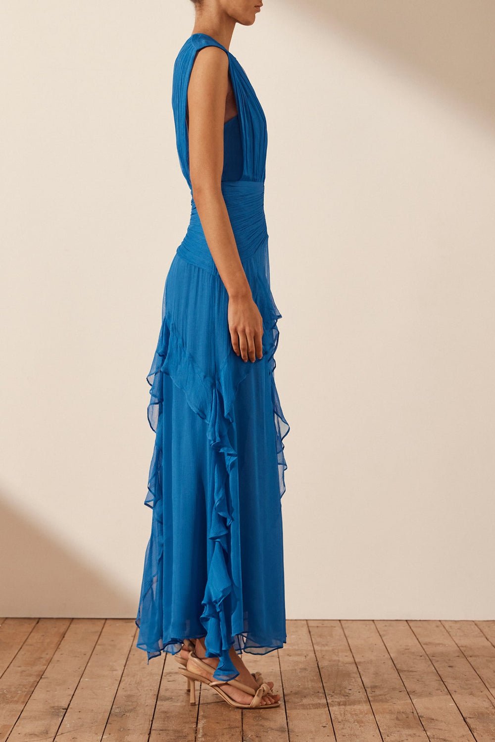 Blue - A woman wearing a vibrant cobalt blue sleeveless chiffon maxi dress featuring a high gathered neckline, a wide ruched waistband, and cascading vertical ruffles along the skirt.