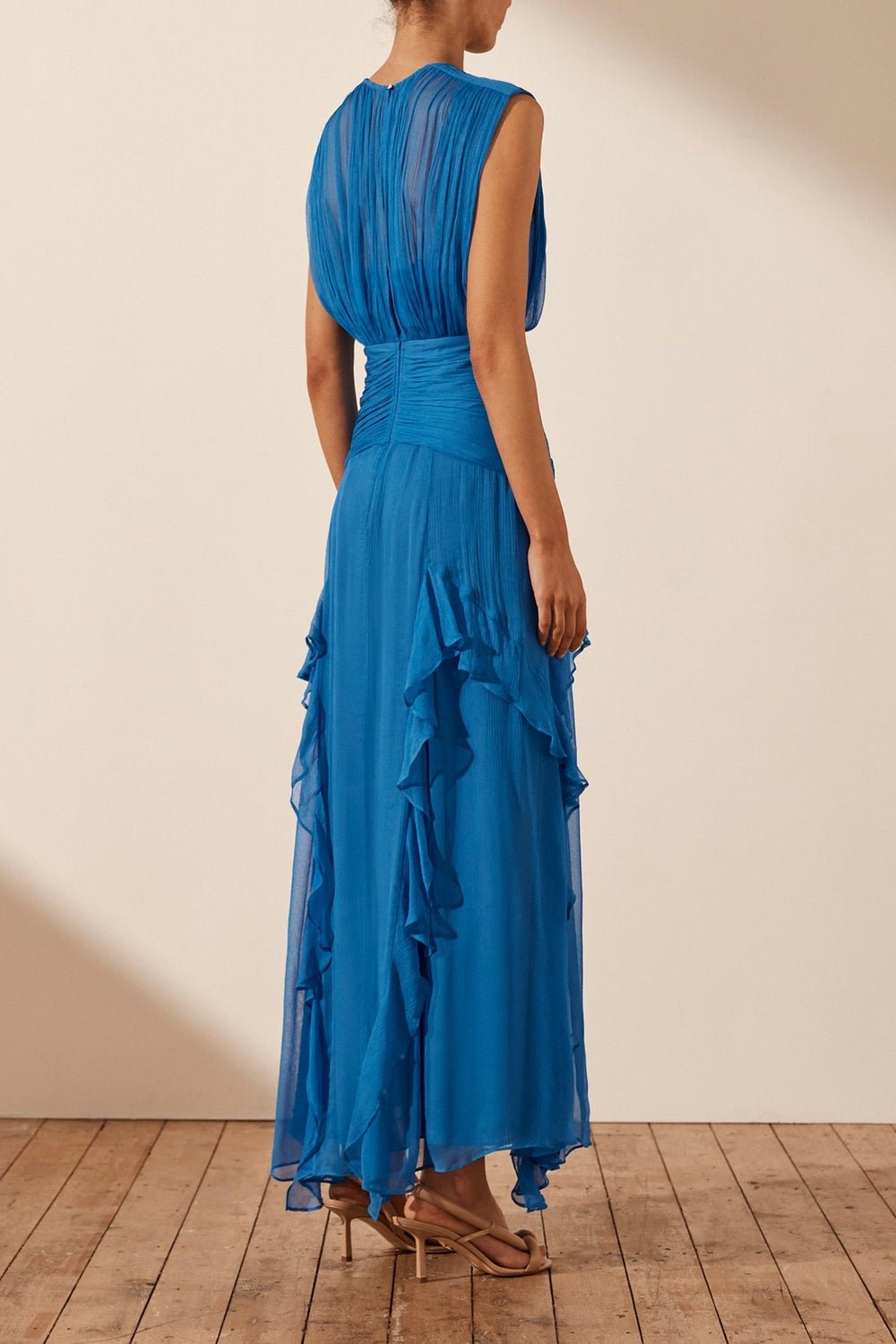 Blue - A woman wearing a vibrant cobalt blue sleeveless chiffon maxi dress featuring a high gathered neckline, a wide ruched waistband, and cascading vertical ruffles along the skirt.