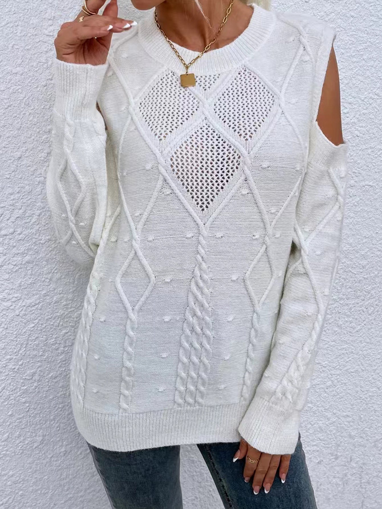 White - Women's beige long-sleeve knit sweater featuring cold shoulder cutouts, a crew neckline, and a textured cable knit pattern with bobble details, styled casually with blue jeans.