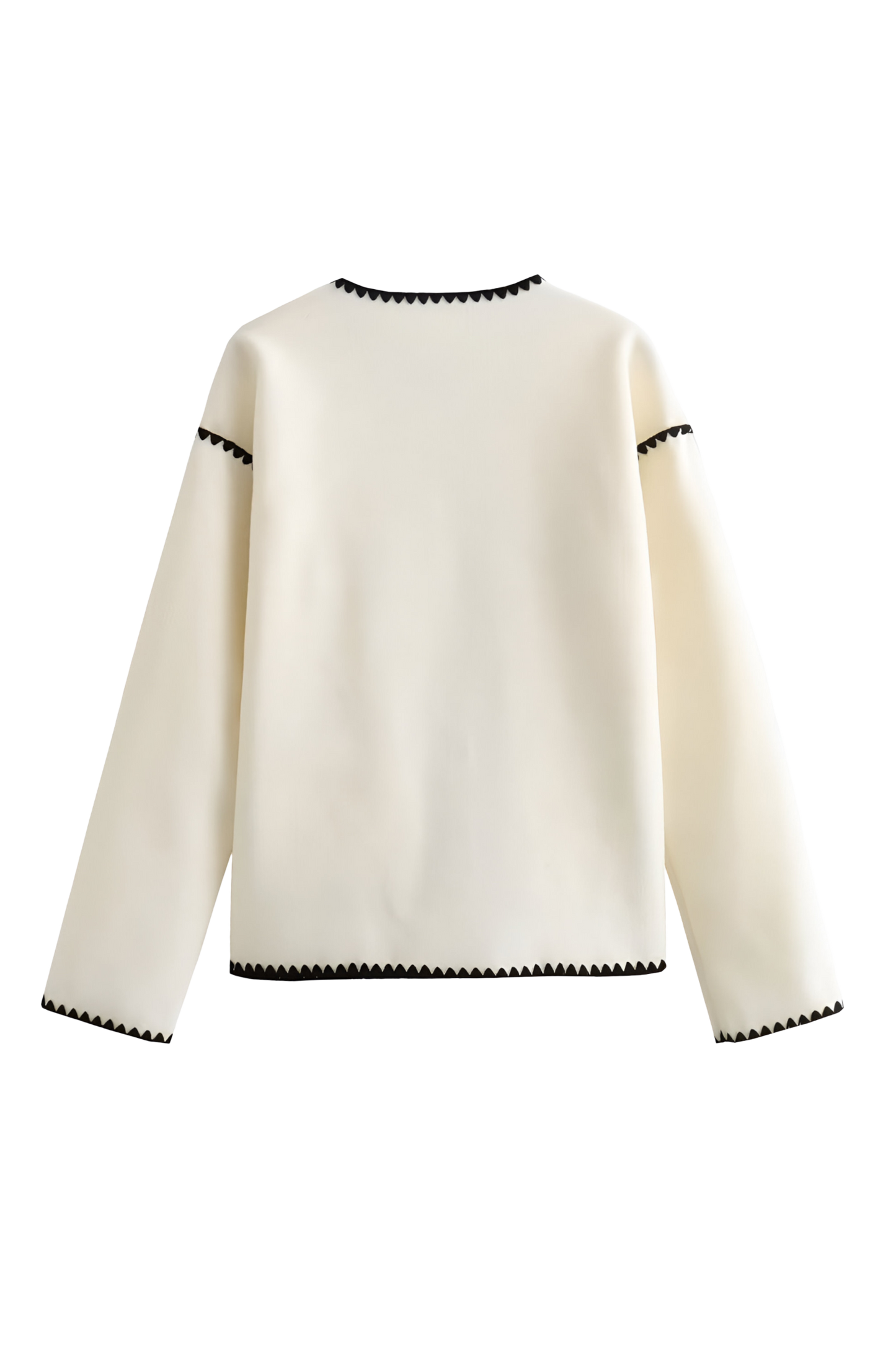 A woman wearing a cream-coloured knit cardigan featuring black contrast stitching along the edges, neckline, and front patch pockets, styled with dark denim jeans.