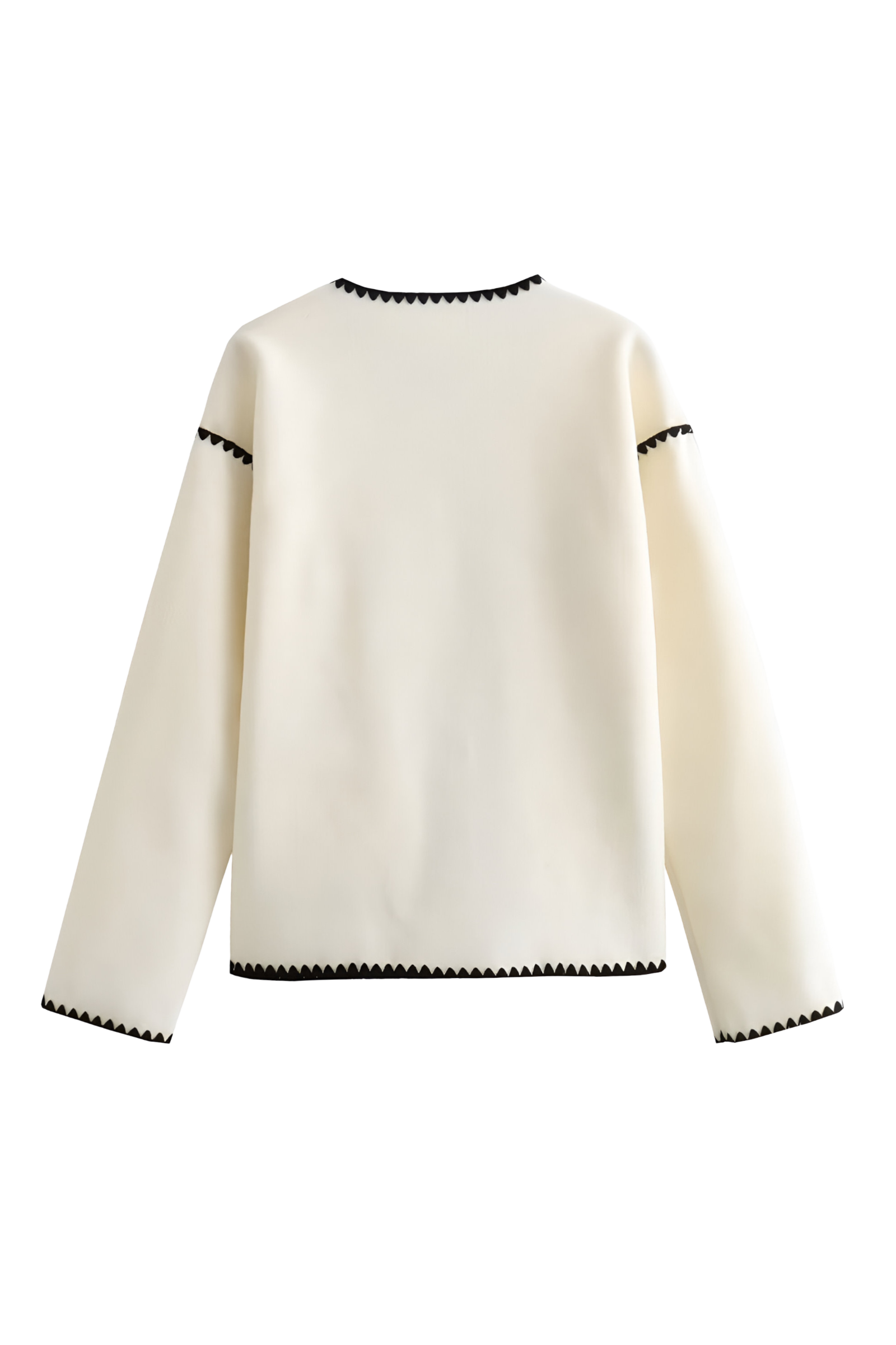 A woman wearing a cream-coloured knit cardigan featuring black contrast stitching along the edges, neckline, and front patch pockets, styled with dark denim jeans.