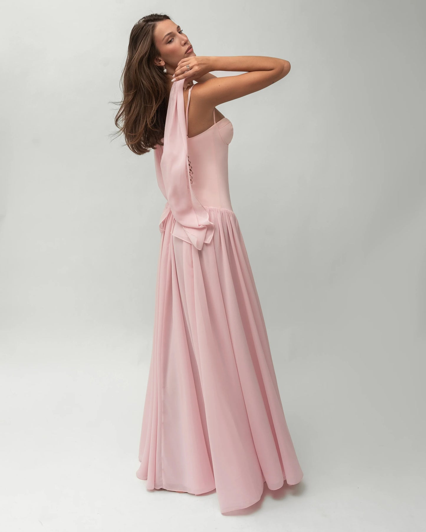 A woman wearing a light pink formal maxi dress featuring a structured corset bodice with spaghetti straps and a flowing, gathered skirt.