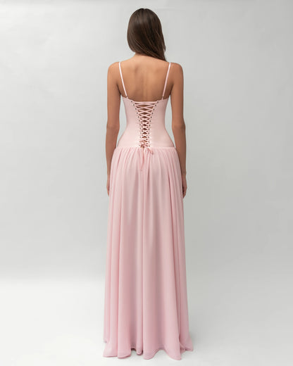 A woman wearing a light pink formal maxi dress featuring a structured corset bodice with spaghetti straps and a flowing, gathered skirt.