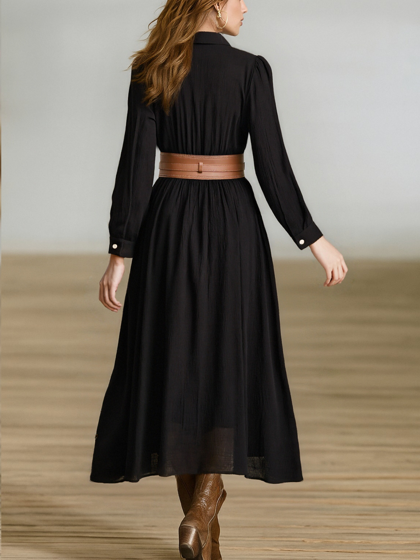 Black - A woman wearing a black, long-sleeved, crinkle-textured maxi shirt dress with a button-down front, styled with a tan leather waist belt and brown embroidered cowboy boots.