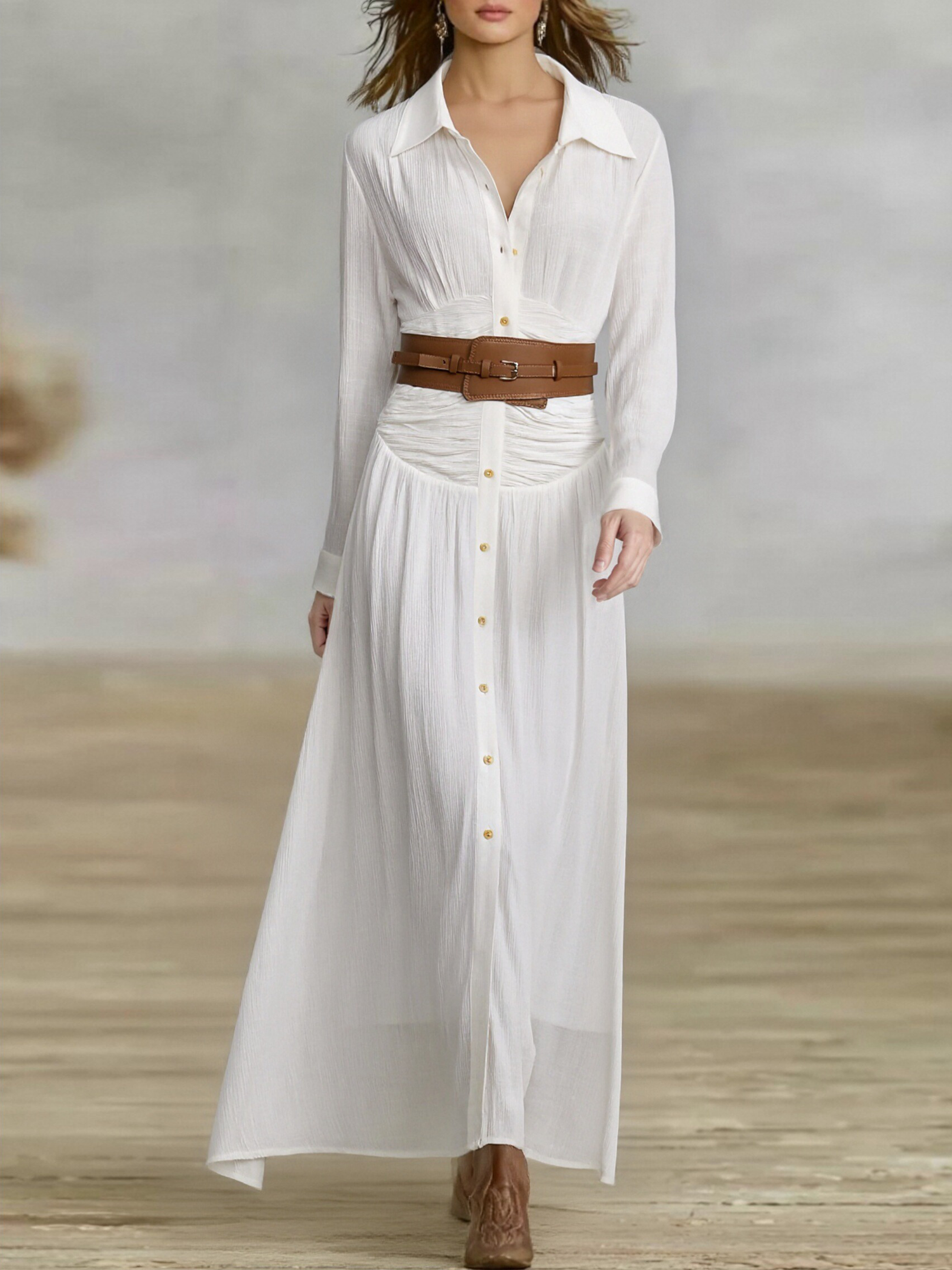 White - A woman wearing a black, long-sleeved, crinkle-textured maxi shirt dress with a button-down front, styled with a tan leather waist belt and brown embroidered cowboy boots.