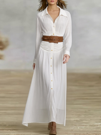 White - A woman wearing a black, long-sleeved, crinkle-textured maxi shirt dress with a button-down front, styled with a tan leather waist belt and brown embroidered cowboy boots.
