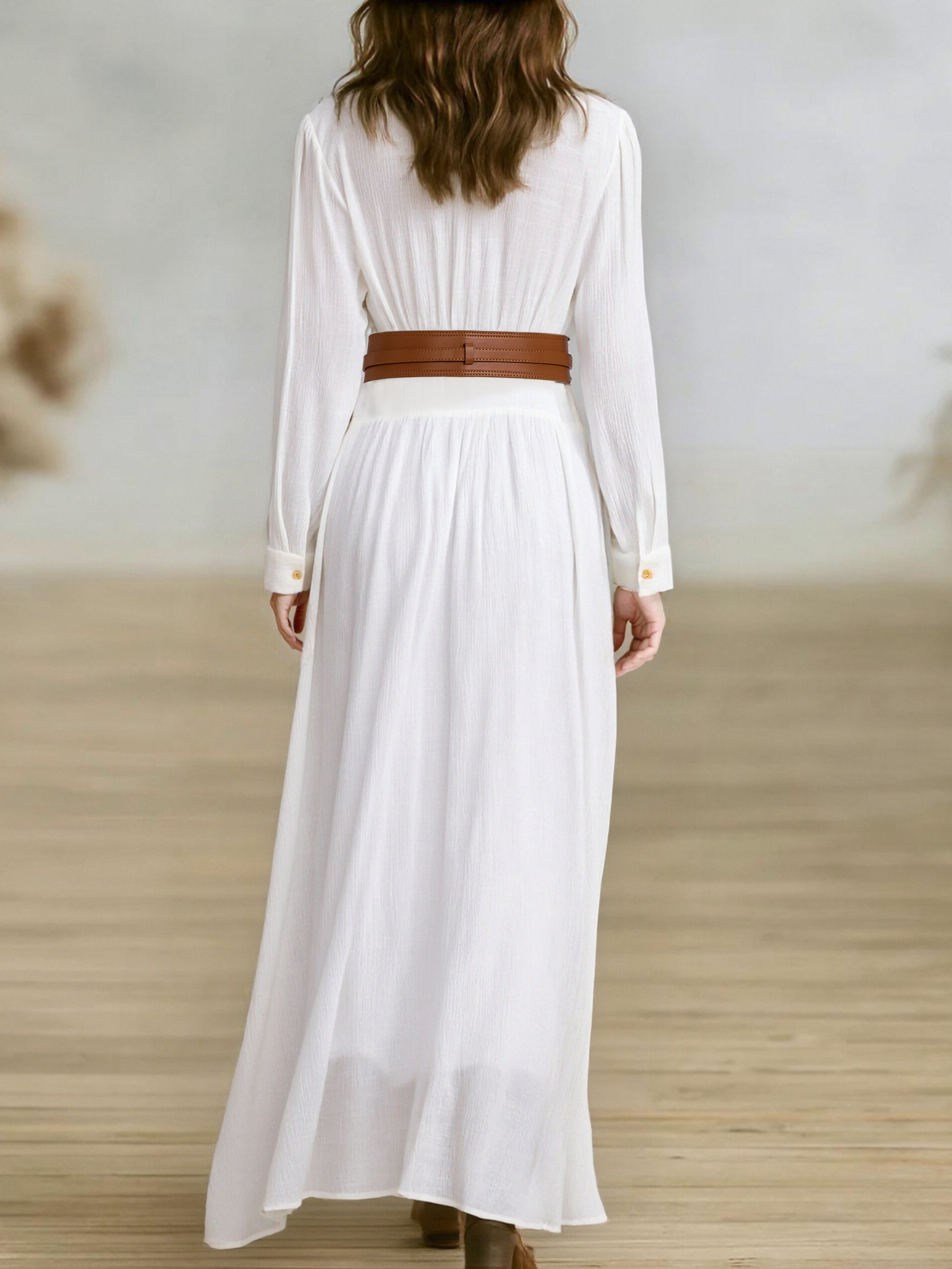 White - A woman wearing a black, long-sleeved, crinkle-textured maxi shirt dress with a button-down front, styled with a tan leather waist belt and brown embroidered cowboy boots.