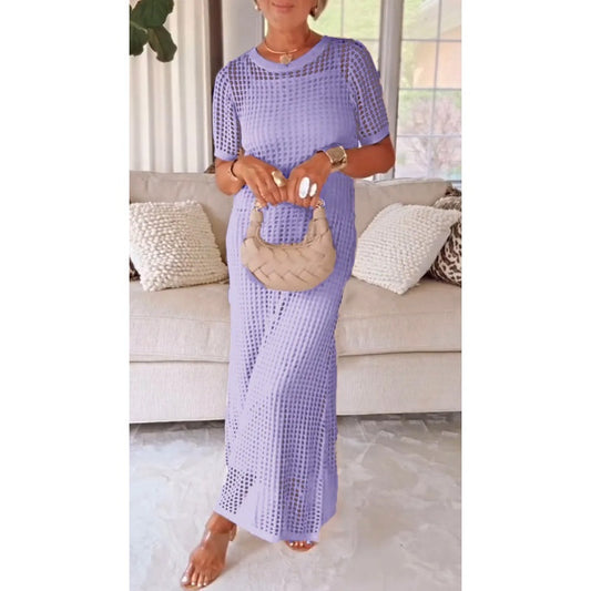Purple - A woman wearing a lavender open-knit crochet maxi dress with a crew neck and short sleeves, styled with a beige woven handbag and gold accessories.