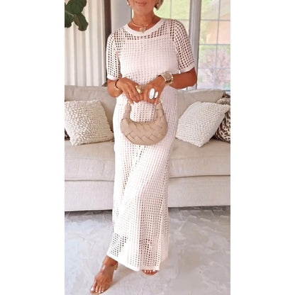 White - A woman wearing a lavender open-knit crochet maxi dress with a crew neck and short sleeves, styled with a beige woven handbag and gold accessories.