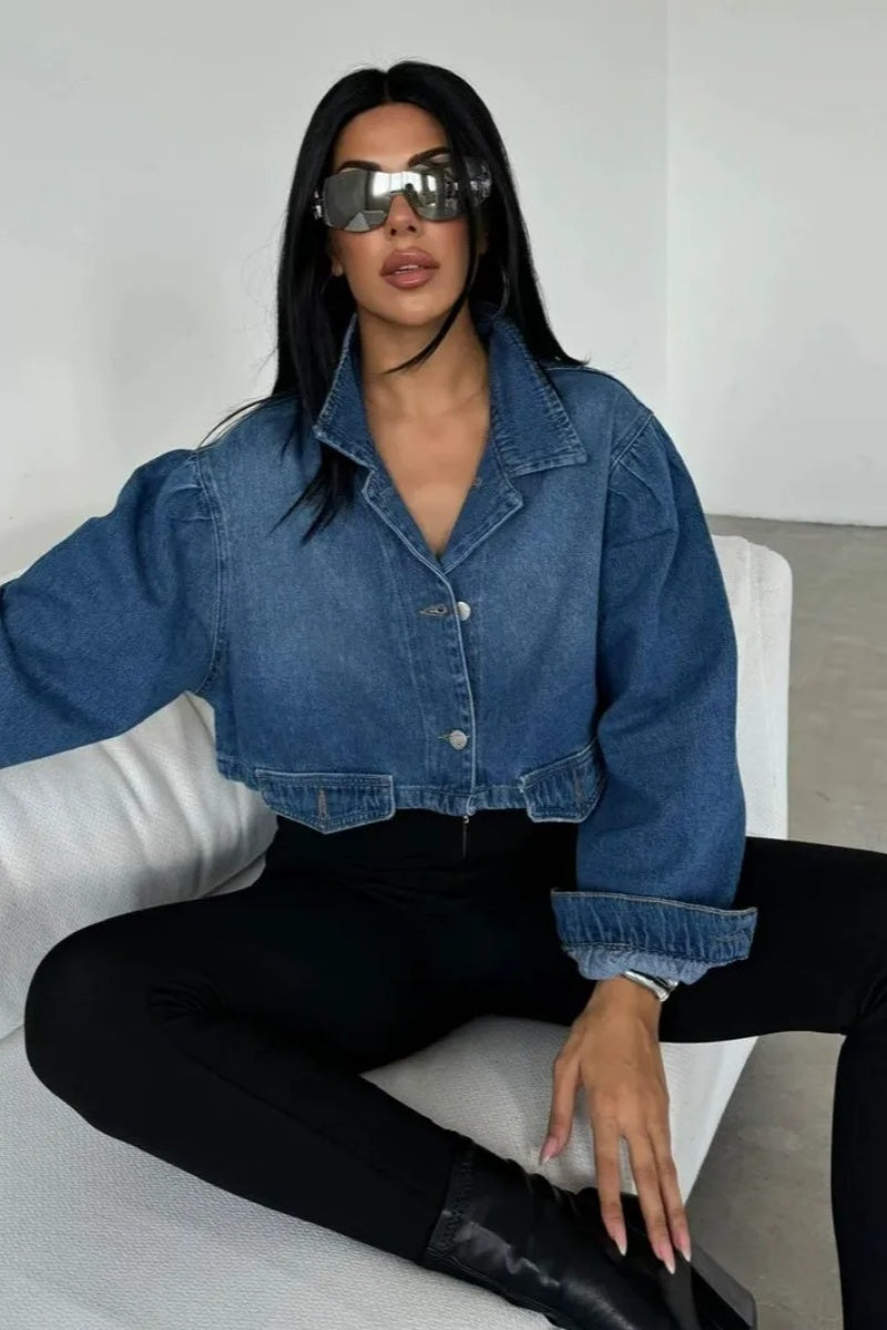Blue - Women's cropped denim jacket featuring voluminous puff sleeves, a classic collar, and a faded wash, styled open over a black top and high-waisted pants.