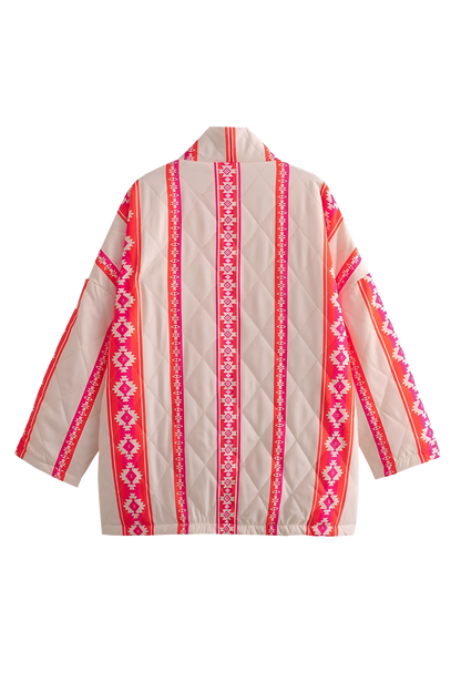 A woman wearing a relaxed, open-front kimono jacket featuring a vibrant pink and orange geometric Aztec print over a cream base, styled over a crochet crop top and shorts.
