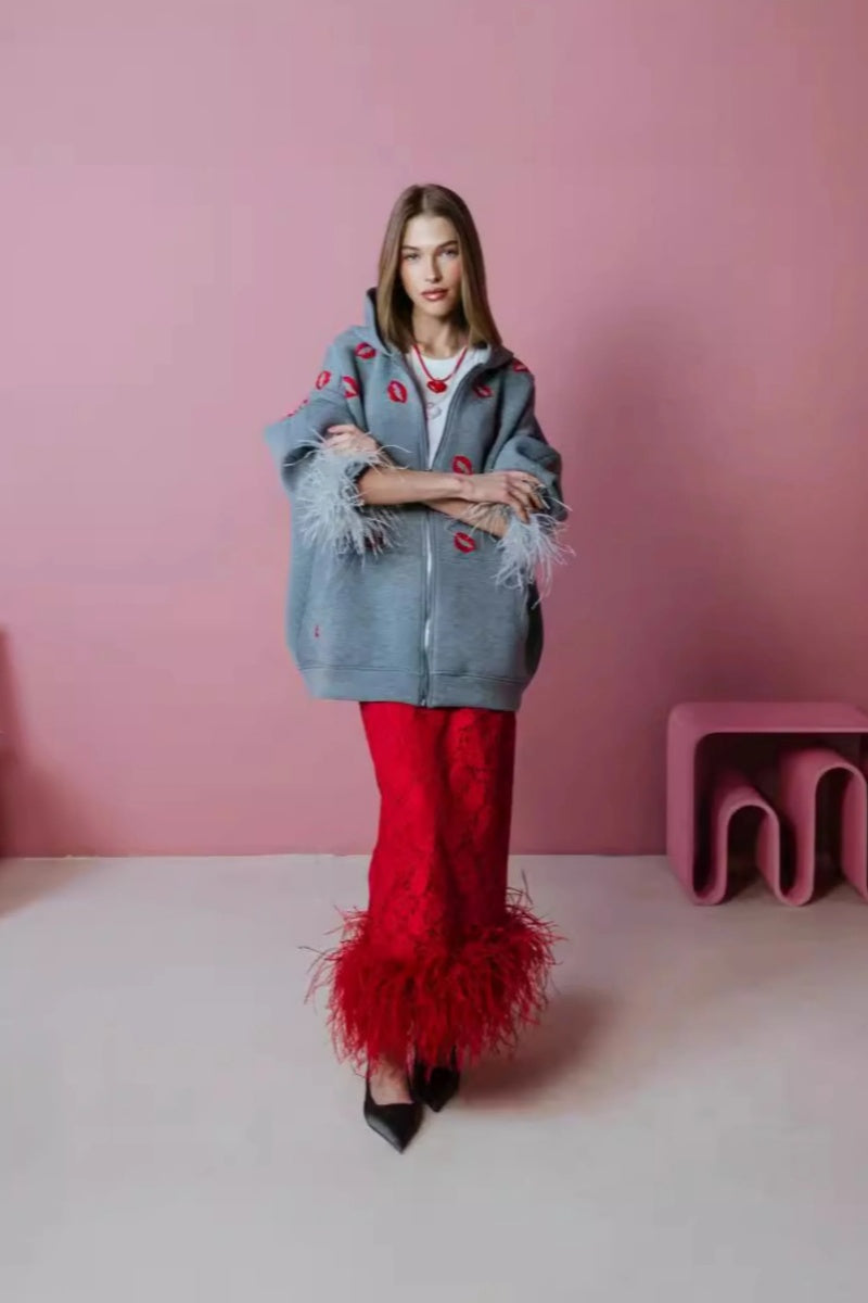 Grey - A woman wearing an oversized grey zip-up hoodie featuring a red lip print and dramatic grey feather cuffs, styled over a white top and red textured skirt.
