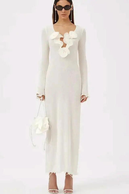 White - A woman wearing a long-sleeved, white ribbed knit maxi dress featuring a deep plunging neckline decorated with large 3D floral appliqués.