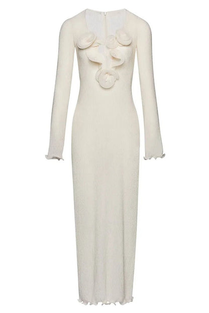 White - A woman wearing a long-sleeved, white ribbed knit maxi dress featuring a deep plunging neckline decorated with large 3D floral appliqués.