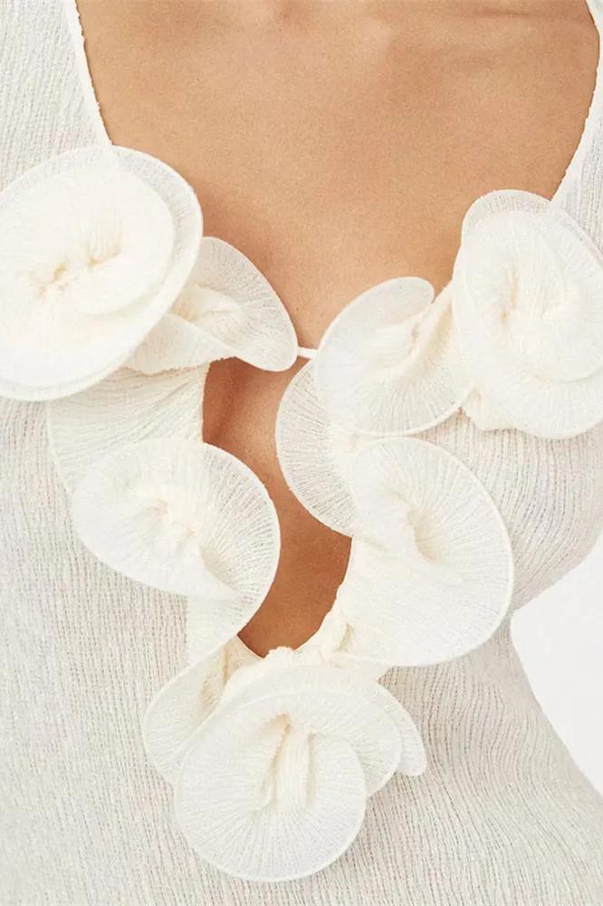 White - A woman wearing a long-sleeved, white ribbed knit maxi dress featuring a deep plunging neckline decorated with large 3D floral appliqués.