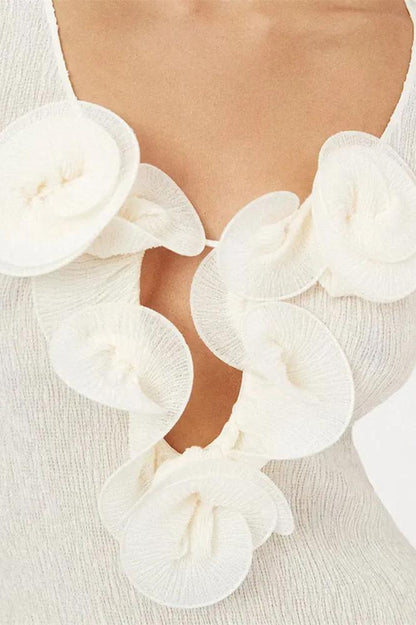 White - A woman wearing a long-sleeved, white ribbed knit maxi dress featuring a deep plunging neckline decorated with large 3D floral appliqués.