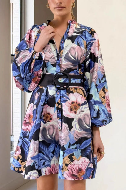 A woman modeling a woven floral long-sleeve mini shirtdress featuring a button-down front, voluminous balloon sleeves, and a wide waist belt with a large circular buckle.