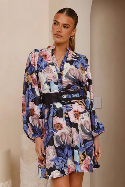Blue - A woman modeling a woven floral long-sleeve mini shirtdress featuring a button-down front, voluminous balloon sleeves, and a wide waist belt with a large circular buckle.