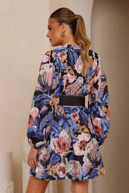 Blue - A woman modeling a woven floral long-sleeve mini shirtdress featuring a button-down front, voluminous balloon sleeves, and a wide waist belt with a large circular buckle.