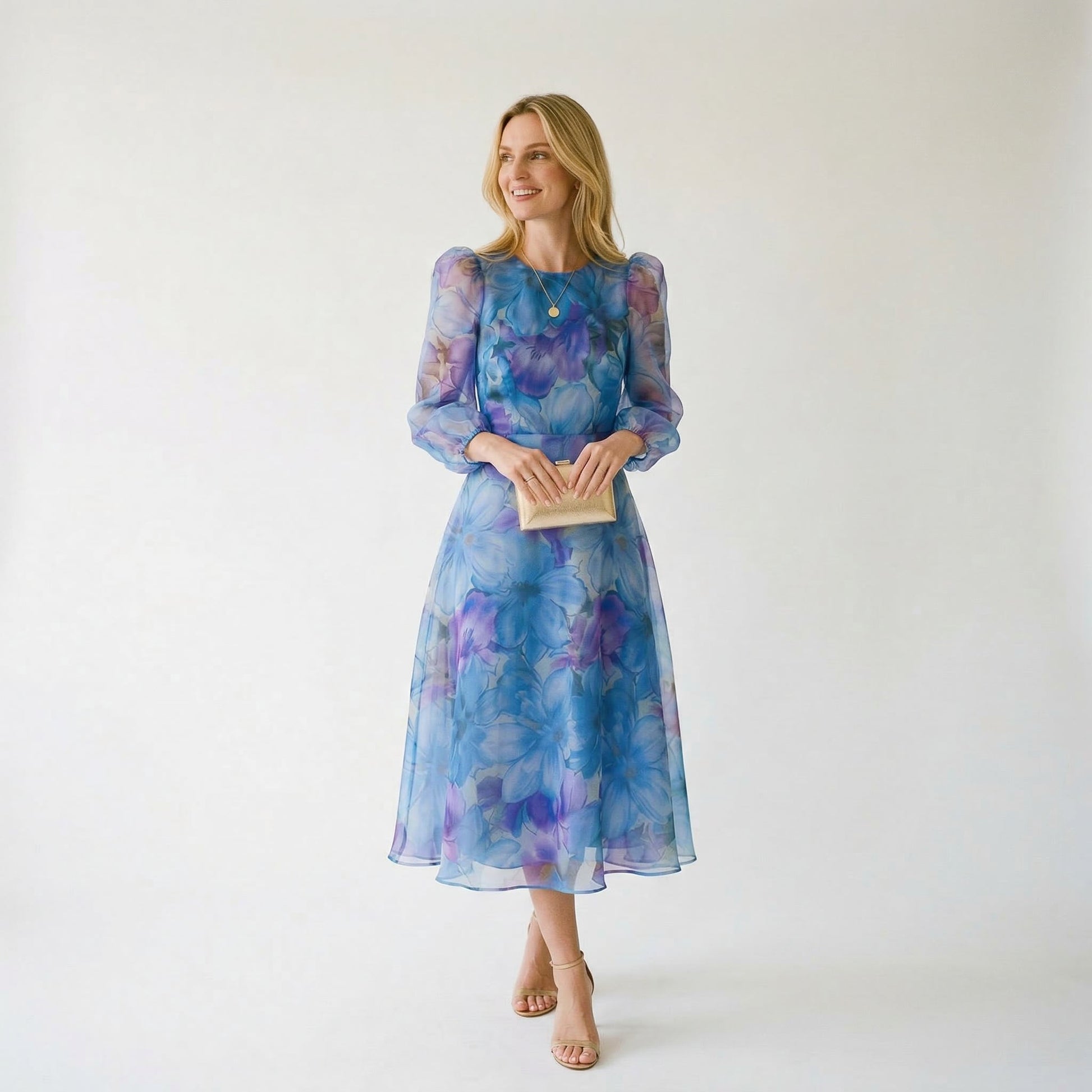 Blue - A woman stands wearing a blue and purple floral print chiffon midi dress with long sheer puff sleeves, a high neckline, and an A-line skirt, holding a gold clutch.