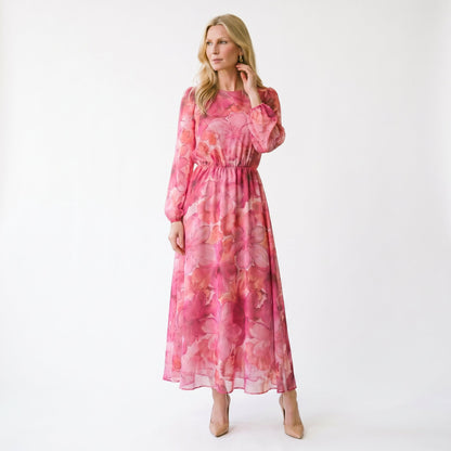 Pink - A woman stands wearing a blue and purple floral print chiffon midi dress with long sheer puff sleeves, a high neckline, and an A-line skirt, holding a gold clutch.