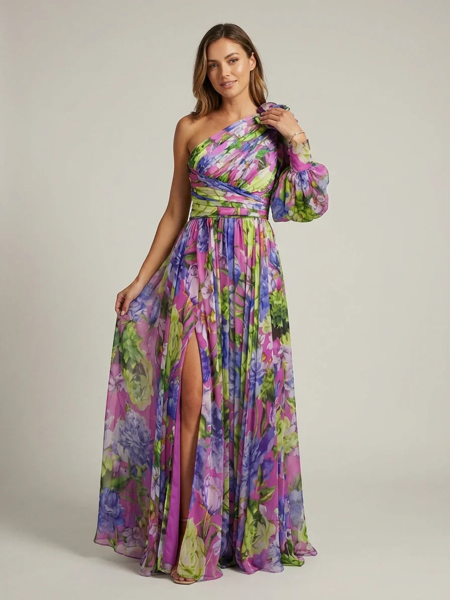 A woman wearing a vibrant floral print chiffon one-shoulder maxi dress with a single long balloon sleeve, ruched bodice, and a high leg slit.