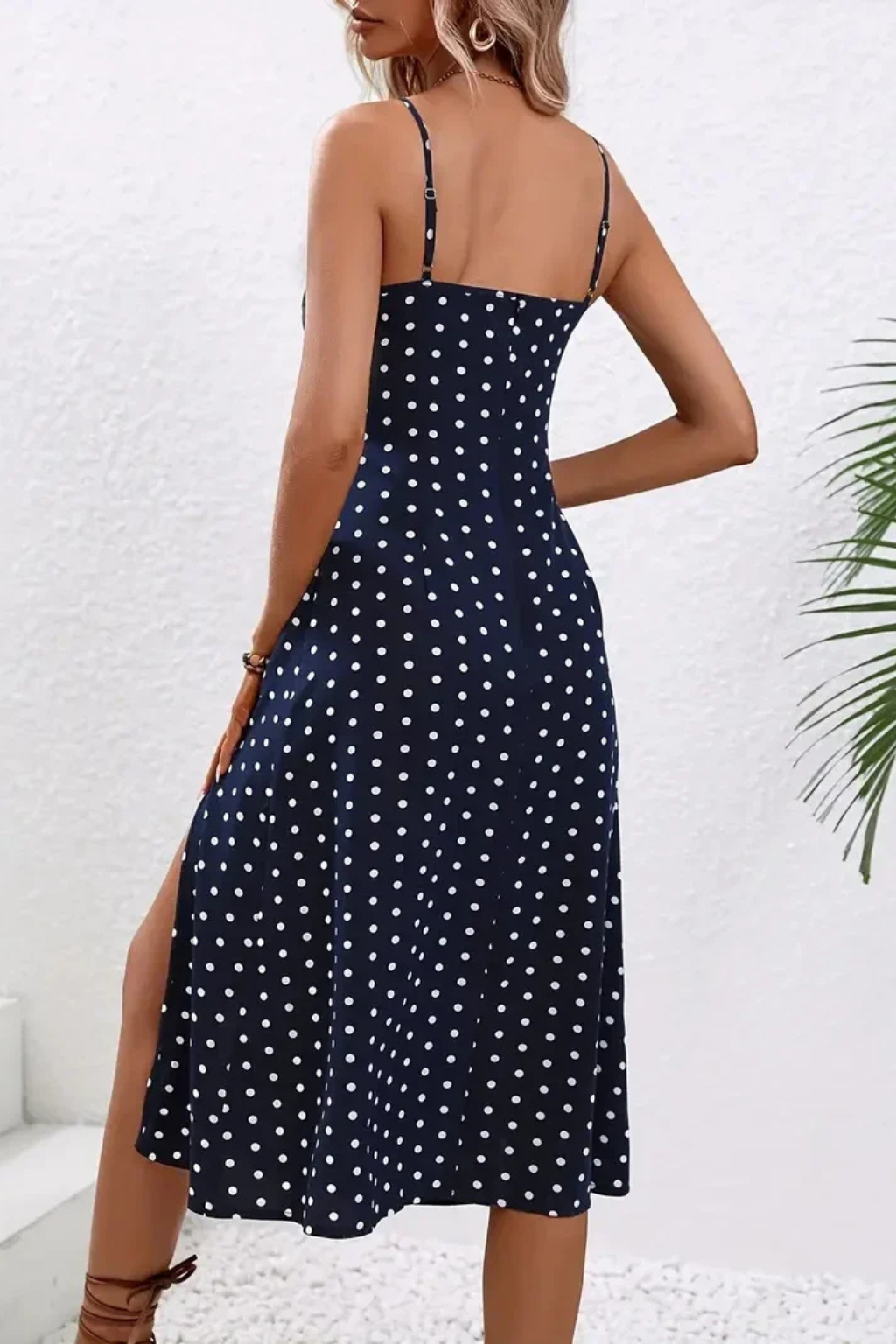 Green Dot - A woman wearing a black midi-length slip dress with a delicate red and white floral print, featuring thin spaghetti straps, a ruched bust, and a high front slit.