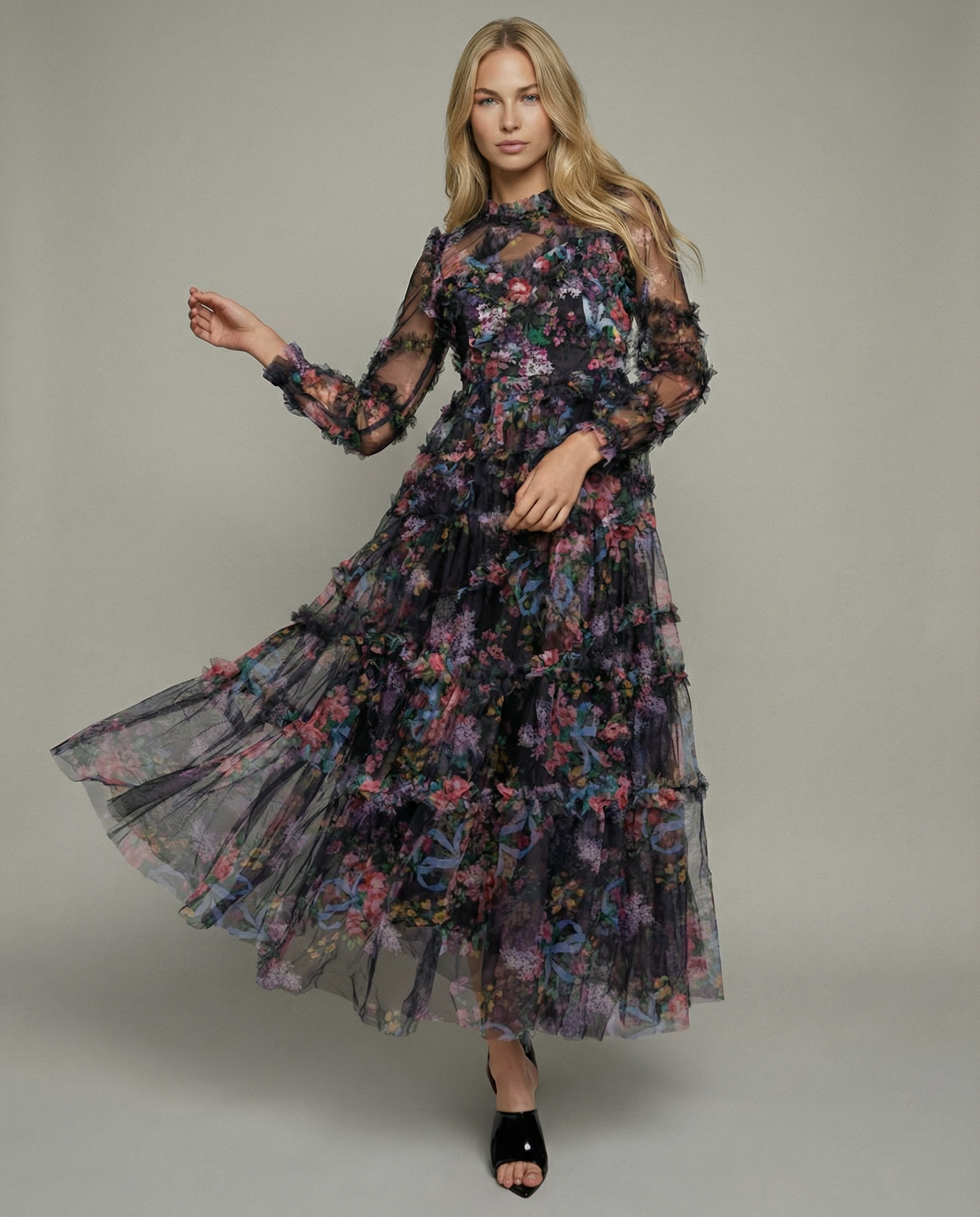 Black - A model wearing a high-neck, long-sleeved maxi dress in black tulle with a vibrant multi-coloured floral print, featuring tiered ruffles and sheer sleeves.