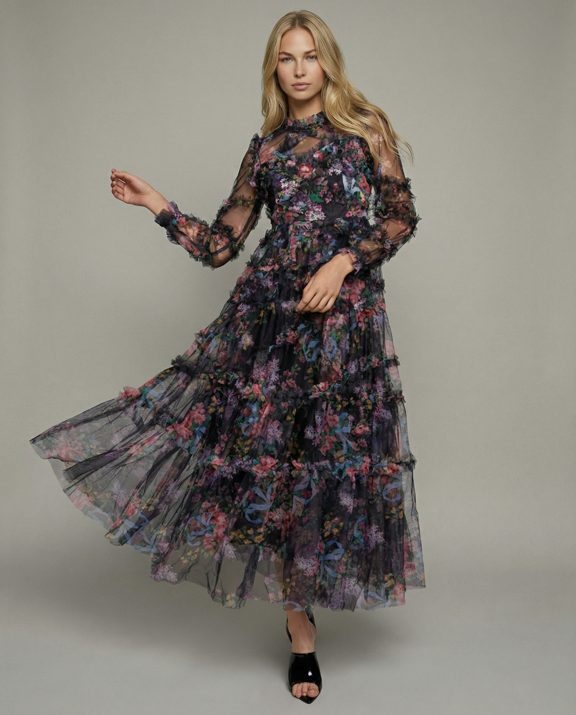 Black - A model wearing a high-neck, long-sleeved maxi dress in black tulle with a vibrant multi-coloured floral print, featuring tiered ruffles and sheer sleeves.