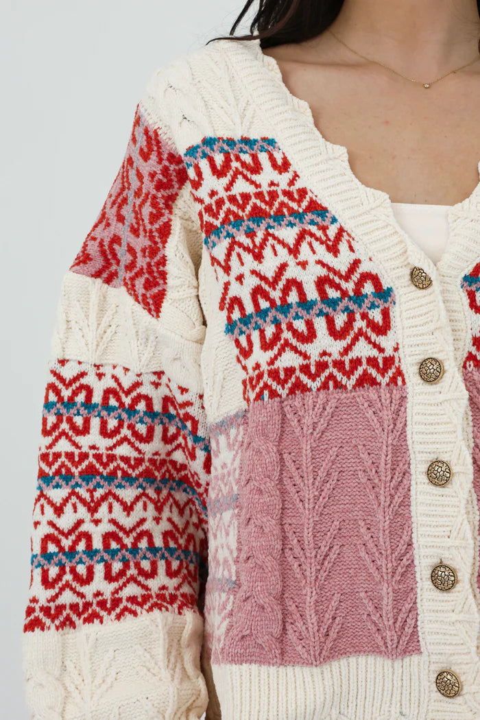 Multi-color - Women's chunky V-neck cardigan featuring a patchwork design of pink, red, and cream Fair Isle patterns and cable knit textures, finished with scalloped edges and metallic buttons.