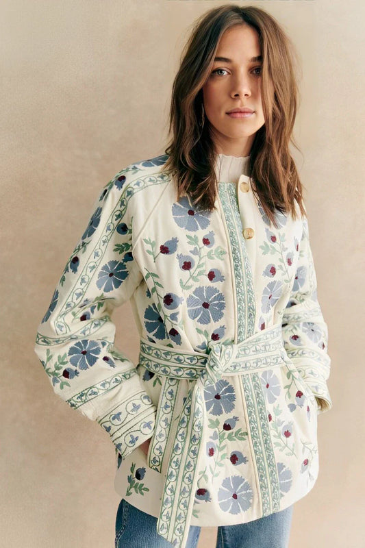 Blue - Women's cream mid-length jacket featuring blue and burgundy floral embroidery, a matching tie-waist belt, and button-front closure, styled over denim.