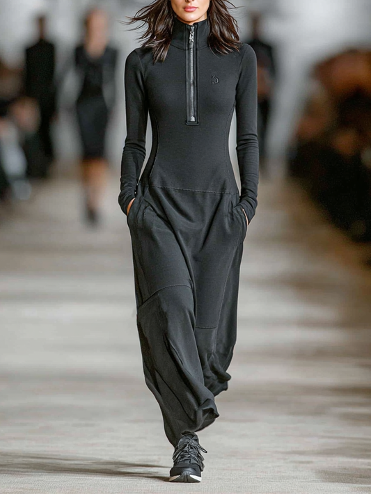 Black - A model walks a runway wearing a black, long-sleeved, high-neck maxi dress with a half-zip front, fitted bodice, dropped waist, and relaxed skirt with side pockets.