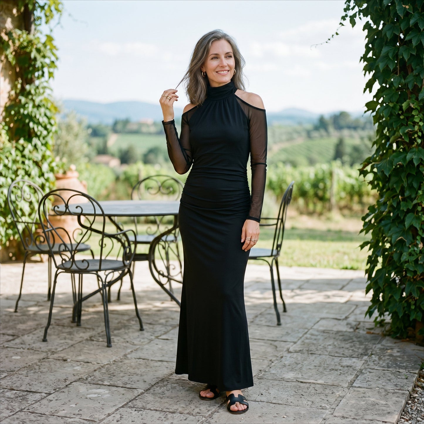 2XL(18) - A woman wearing a floor-length black evening gown featuring a high mock neckline, sheer long mesh sleeves with cold-shoulder cutouts, and a ruched fitted bodice that drapes into a subtle mermaid silhouette.