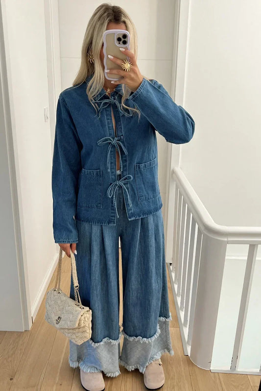 A woman taking a mirror selfie wearing a blue denim jacket featuring three tie-front closures and patch pockets, paired with wide-leg denim trousers.