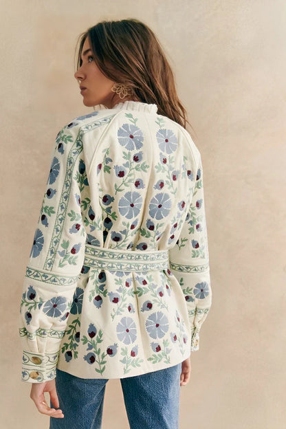 Blue - Women's cream mid-length jacket featuring blue and burgundy floral embroidery, a matching tie-waist belt, and button-front closure, styled over denim.