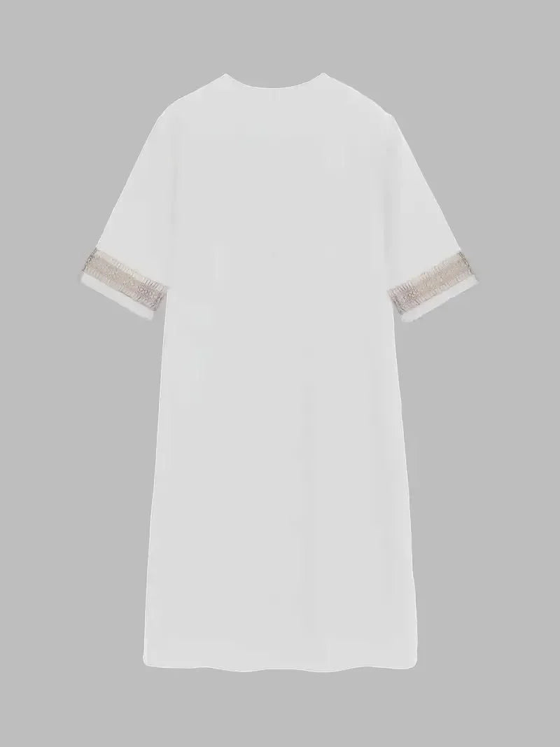 White - A woman wearing a white, knee-length shift dress made of textured linen-like fabric, featuring intricate beige crochet lace trim along the deep V-neckline and elbow-length sleeve cuffs.